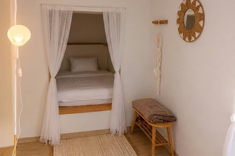 Domeček Mandala — manželská postel ve výklenku za bílými závěsy, lampa, zrcadlo a lavice
